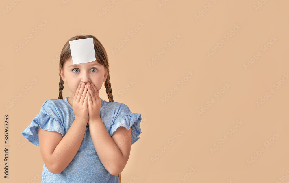 Surprised little girl with blank note paper on her forehead against color background