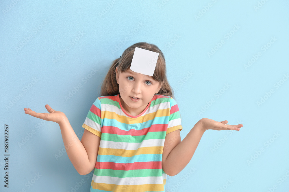 Little girl with blank note paper on her forehead against color background