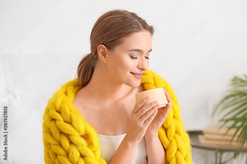 Happy young woman with warm plaid and cup of coffee at home