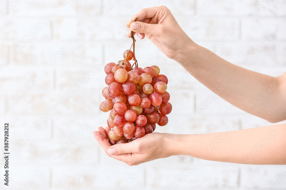 Hands with sweet ripe grapes on light background