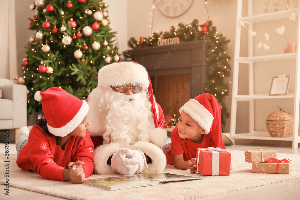 African-American Santa Claus with cute children reading book at home on Christmas eve