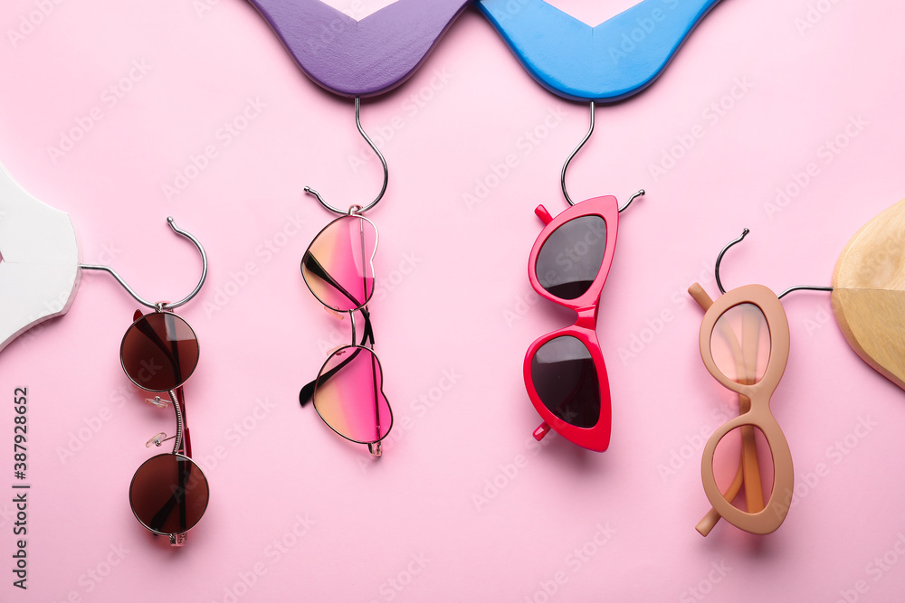 Clothes hangers and sunglasses on color background