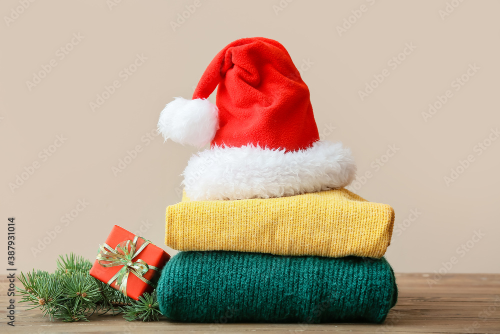 Stylish Christmas clothes with Santa Claus hat on table against color background