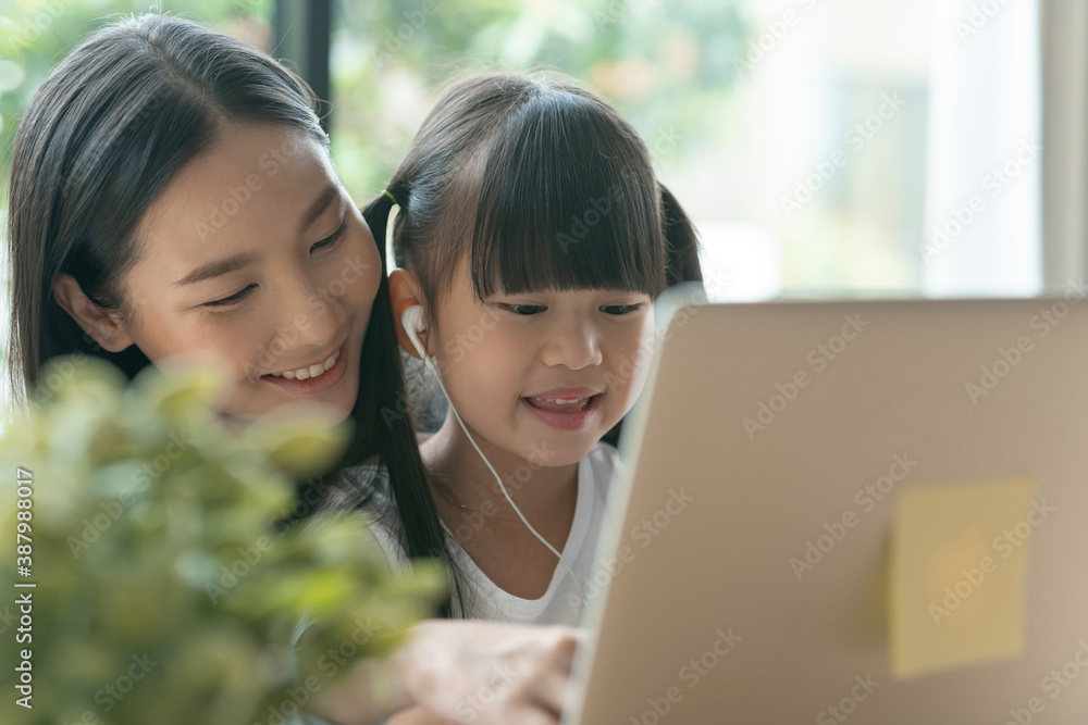 Asian mother enjoy teaching her adorable daughter a homework on a laptop