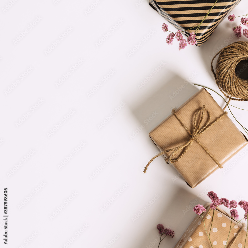 Gift box wrapped in kraft paper and pink flowers on white background. Flat lay styling.