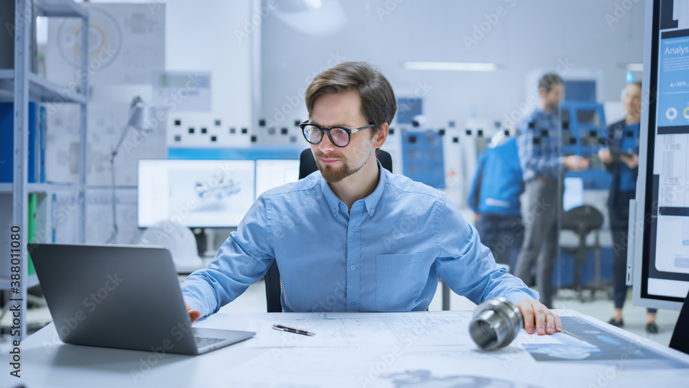 Modern Factory: Industrial Engineer Sitting at His Desk in Workshop, Working on Computer, Redrawing 