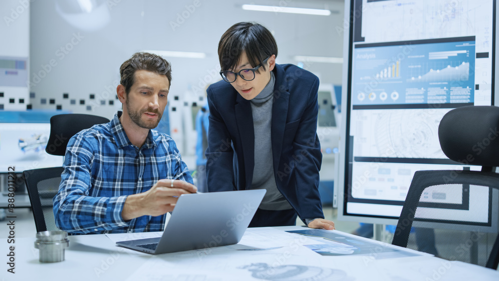 Modern Factory: Industrial Engineer Sitting at His Desk, Working on Laptop Computer, Talks with Chie