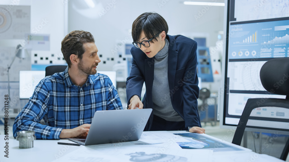 Modern Factory: Industrial Engineer Sitting at His Desk, Working on Laptop Computer, Talks with Chie