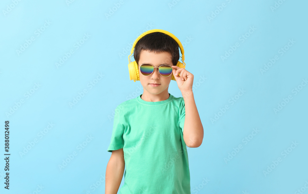 Cute boy with stylish sunglasses listening to music against color background