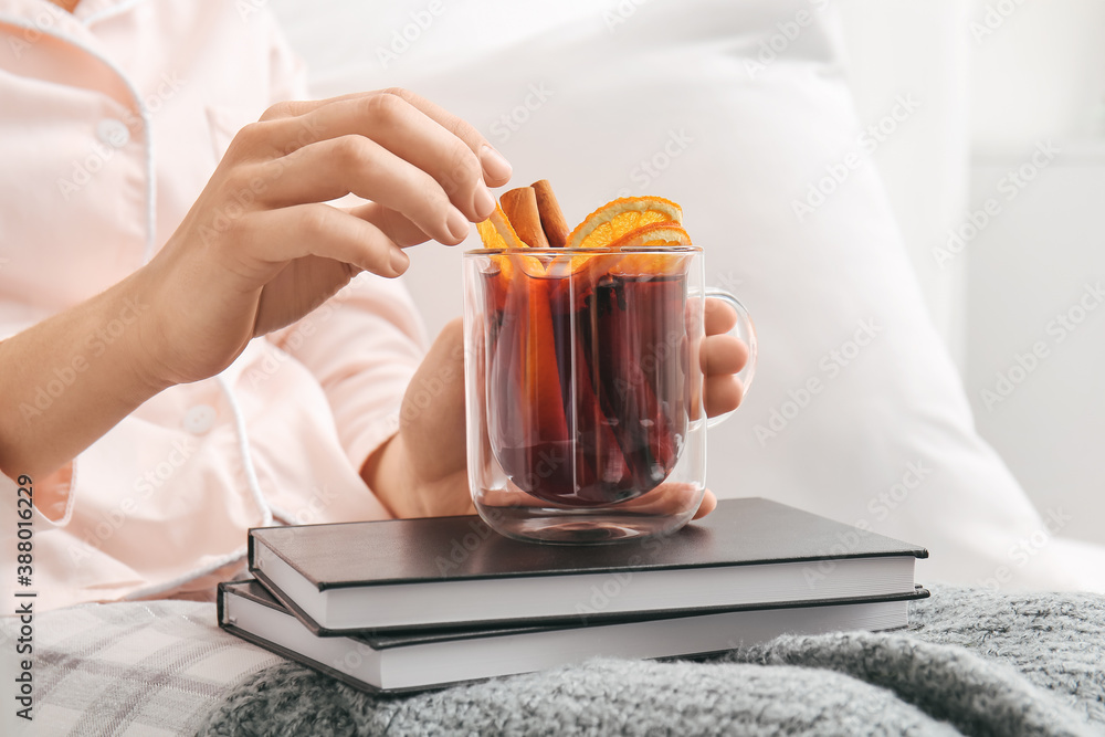 Woman with mulled wine and books in bedroom