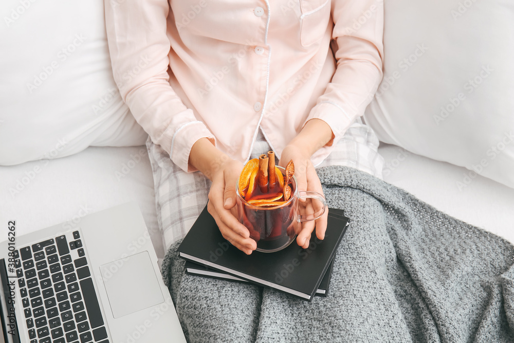 Woman with mulled wine, books and laptop in bedroom