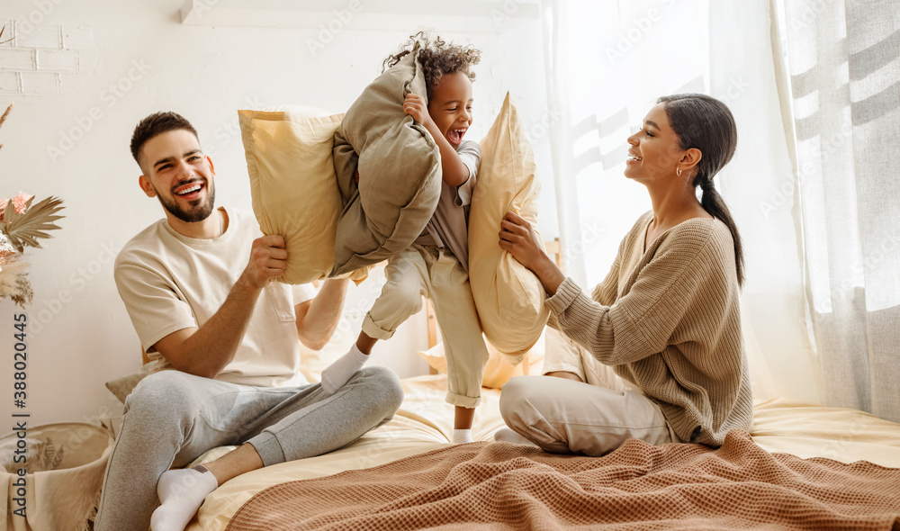 happy multiethnic family mom, dad and child  laughing, playing, fights pillows and jumping in bed   