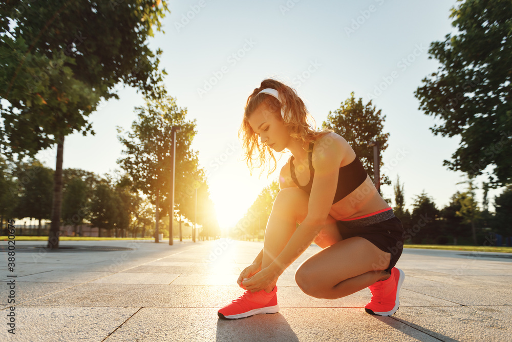 Sporty woman tying laces on sneakers in park.