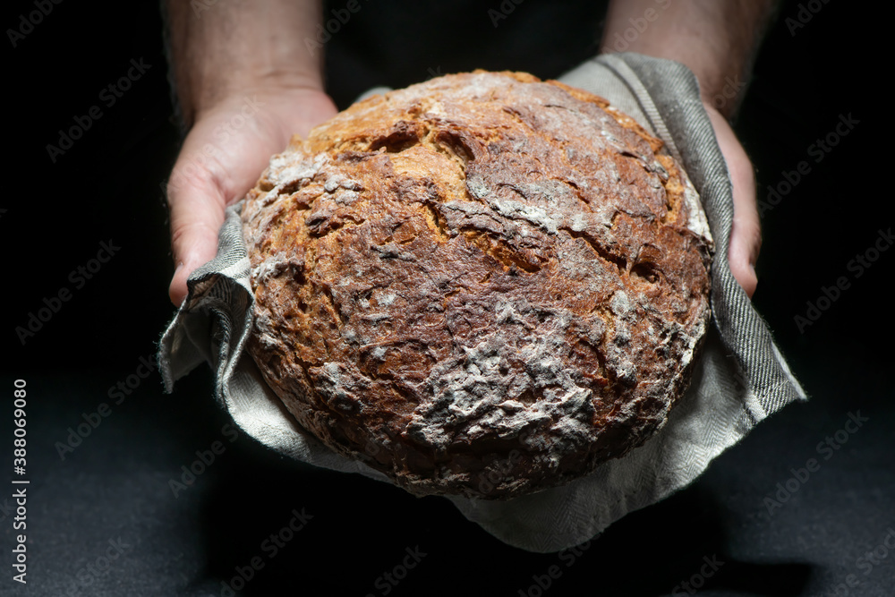 Bakers hands holding and presenting fresh baked loaf of bread