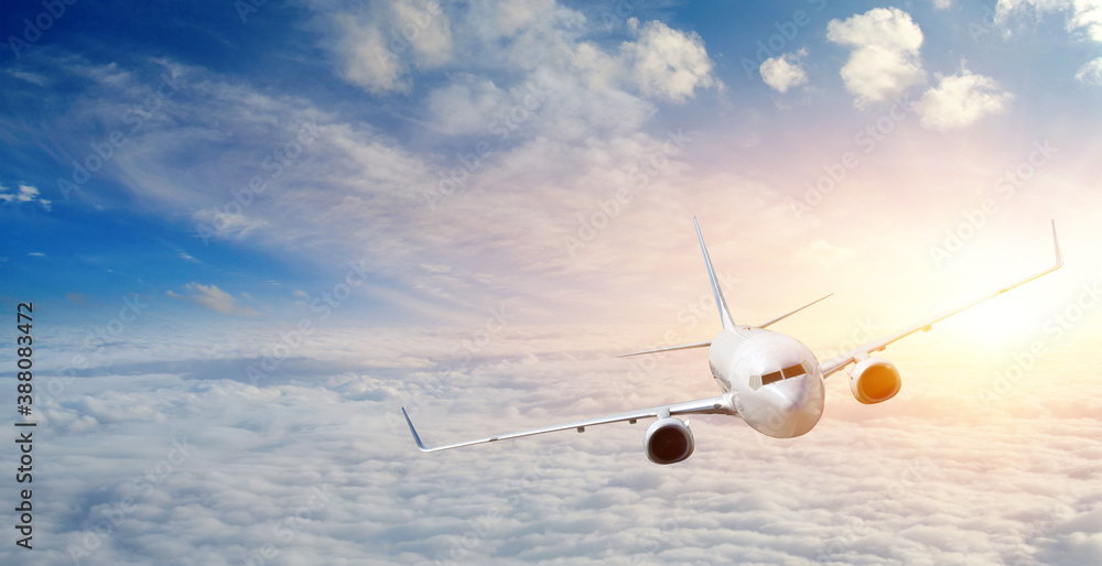 Passengers commercial airplane flying above clouds in sunset.