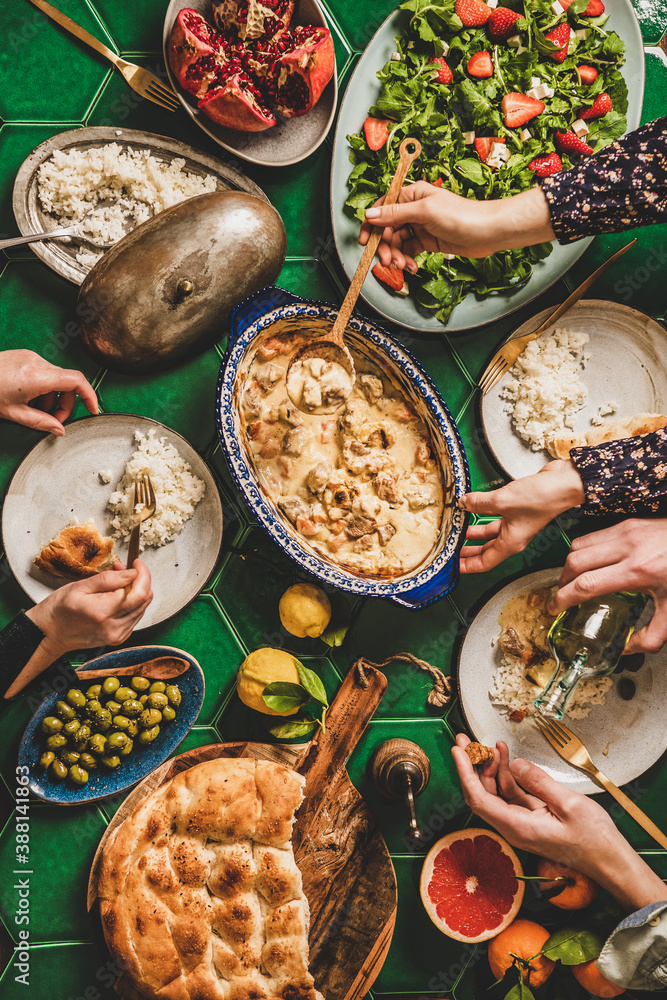 Family having Turkish dinner. Flat-lay of people hands over table with lamb in yogurt sauce, fresh a