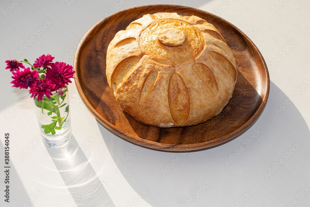 Composition in bright sunlight. Round homemade whole grain bread on a wooden plate and a glass with 