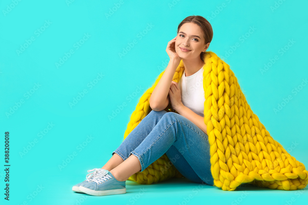 Happy young woman with warm plaid on color background