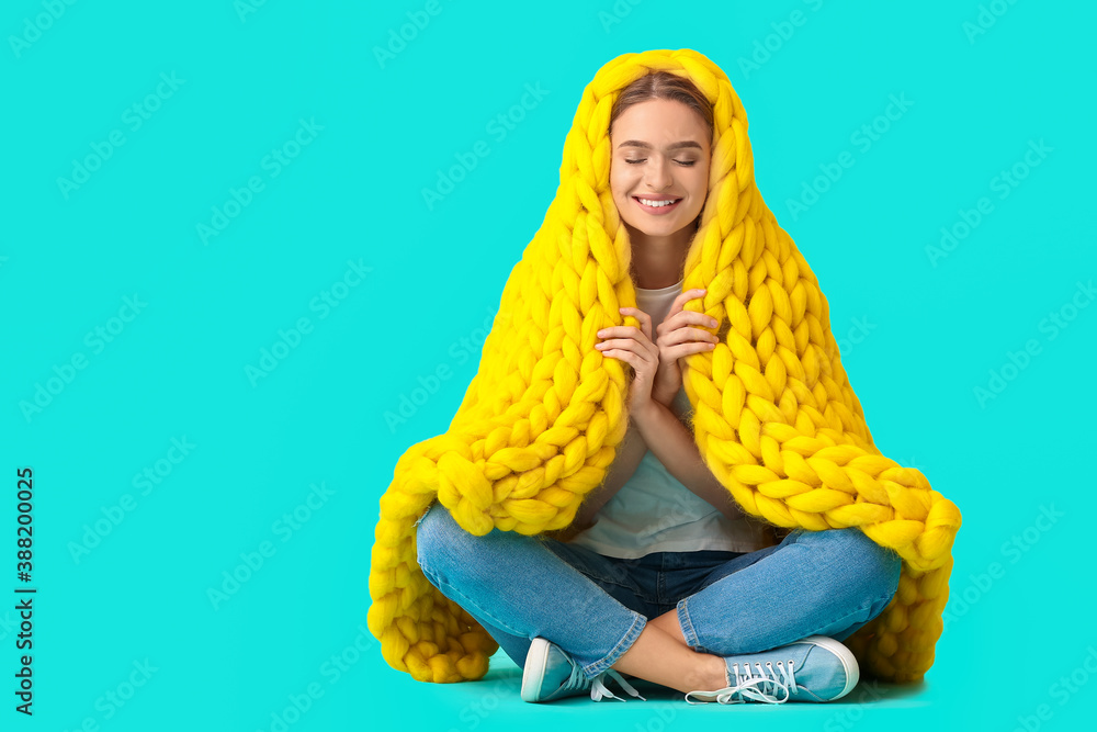 Happy young woman with warm plaid on color background