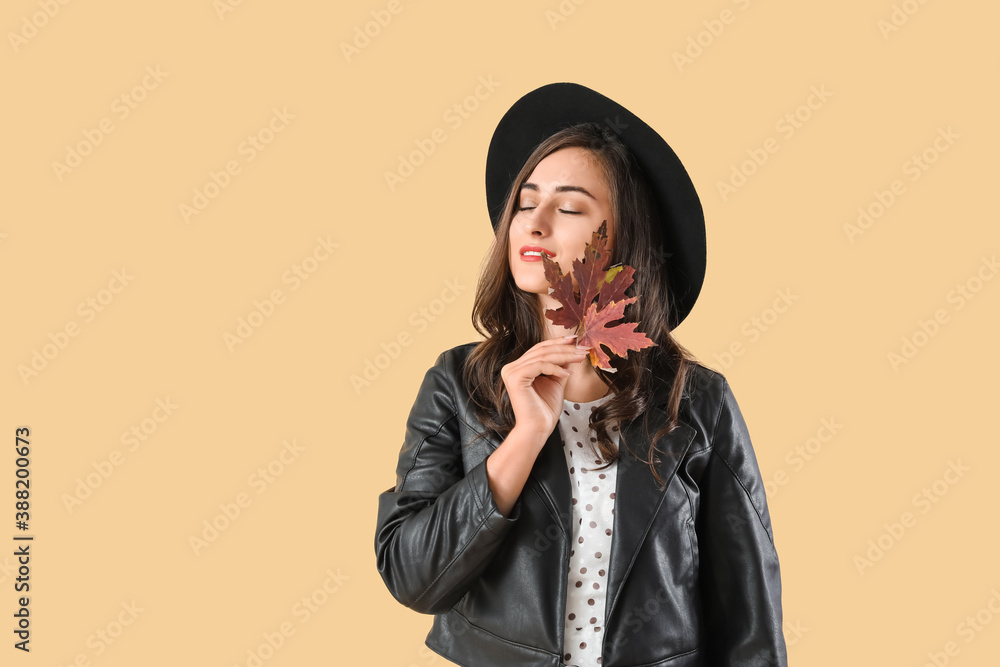 Stylish young woman with autumn leaves on color background