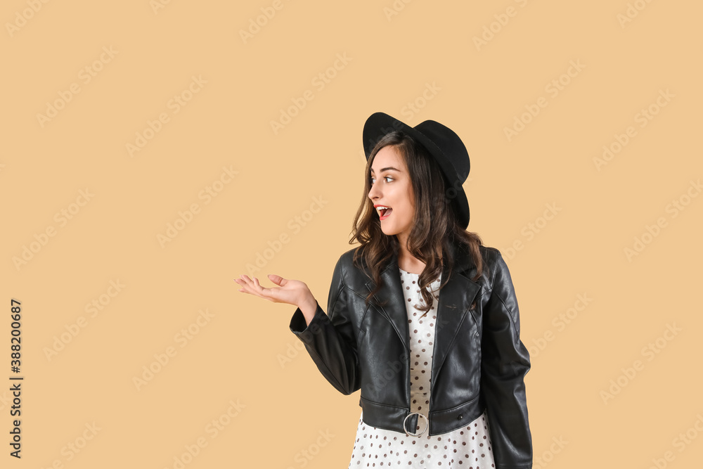 Stylish young woman in autumn clothes showing something on color background