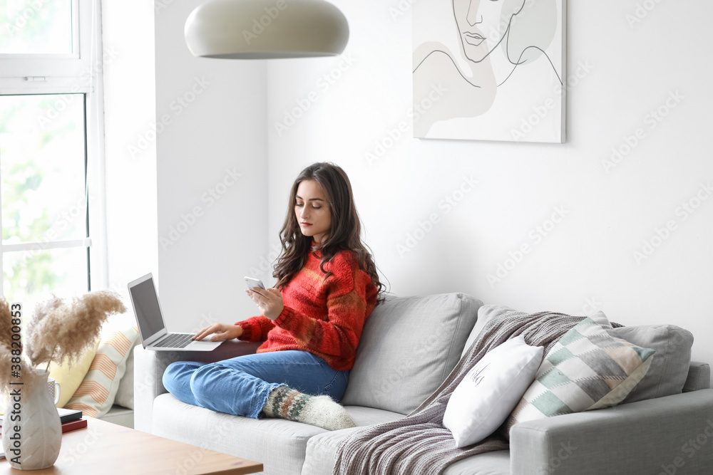 Beautiful young woman with laptop and mobile phone at home