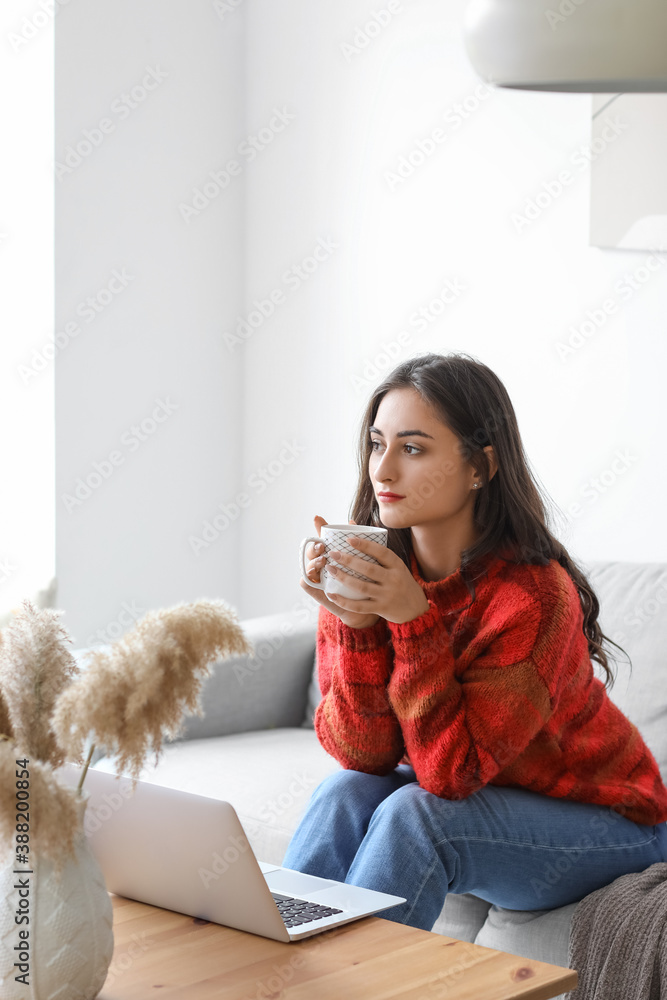 Beautiful young woman with laptop and cup of tea at home