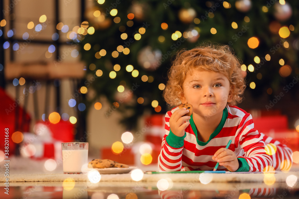 Cute little child eating cookies while writing letter to Santa at home