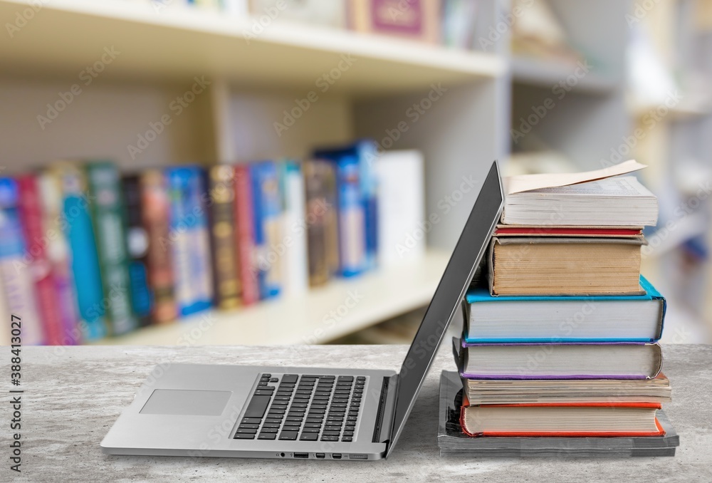 Stack of books with modern laptop on table