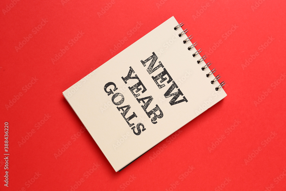 Notebook with text NEW YEAR GOALS on color background