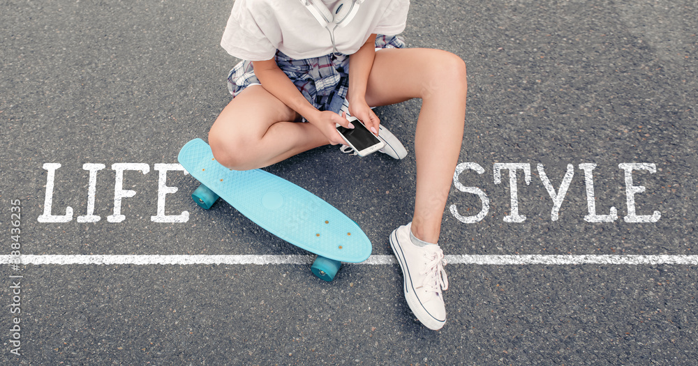 Hipster girl with skateboard, mobile phone and text LIFE STYLE outdoors