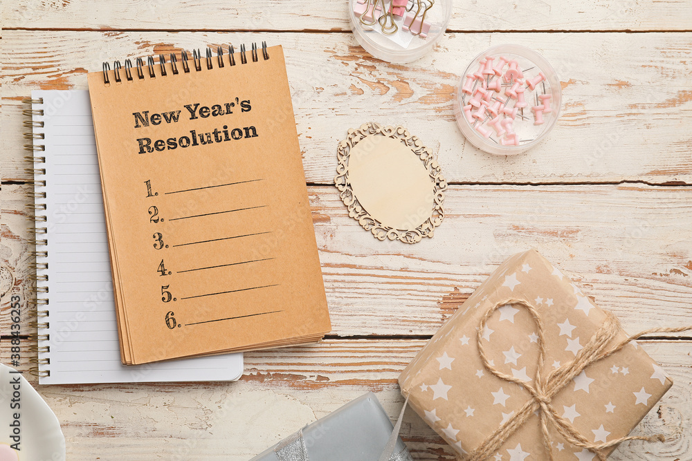 Notebooks with text NEW YEARS RESOLUTION and gift on white wooden background