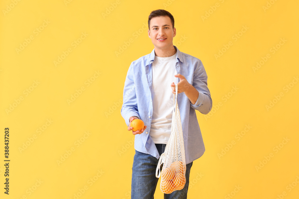 Handsome man with ripe oranges on color background