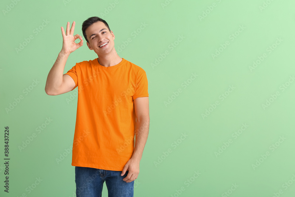 Handsome young man in orange t-shirt showing OK on color background