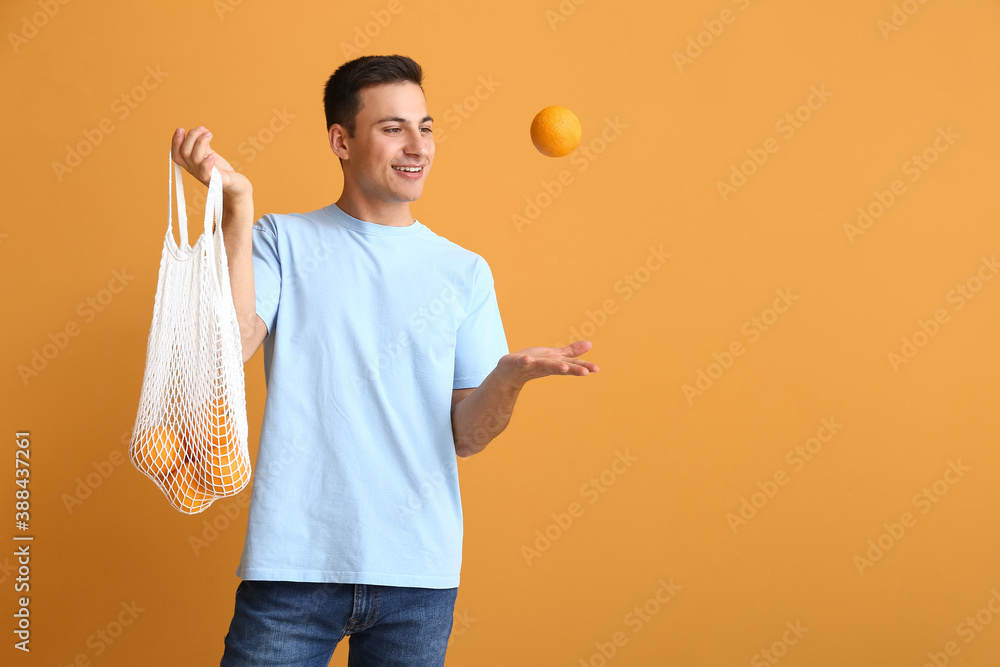 Handsome man with ripe oranges on color background