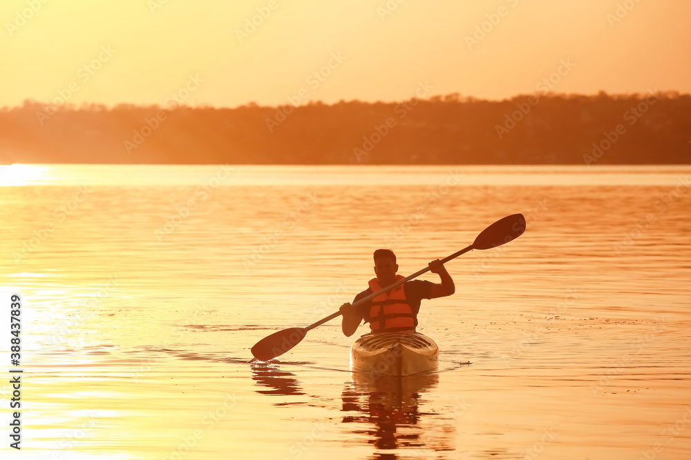 Young man kayaking in river at sunset