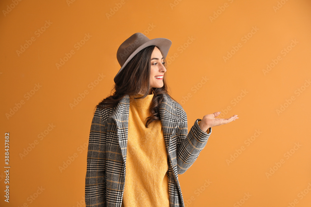 Stylish young woman in autumn clothes showing something on color background