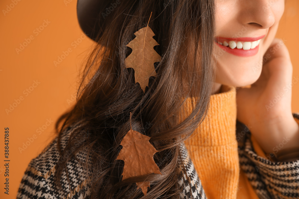 Stylish young woman with autumn leaves on color background, closeup