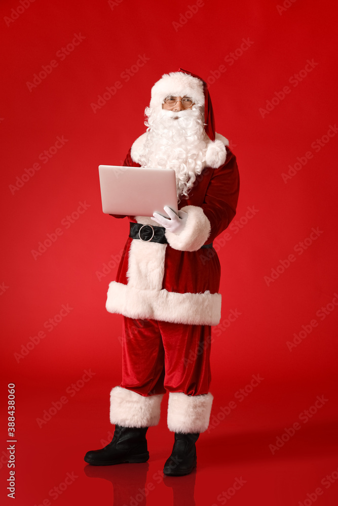 Santa Claus with laptop on color background