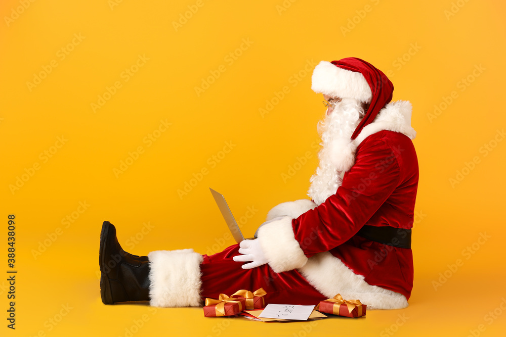 Santa Claus with laptop checking e-mail on color background