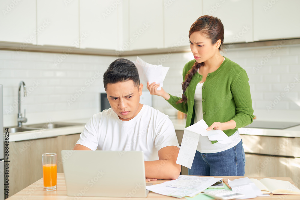 Angry young couple shouting in a hard quarrel by their many debts at home. Financial family problems