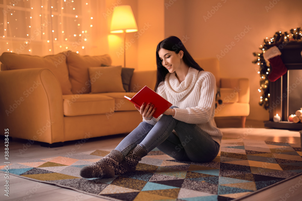 Beautiful young woman reading book at home on Christmas eve