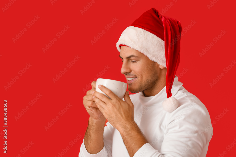 Handsome young man in Santa hat and with hot tea on color background