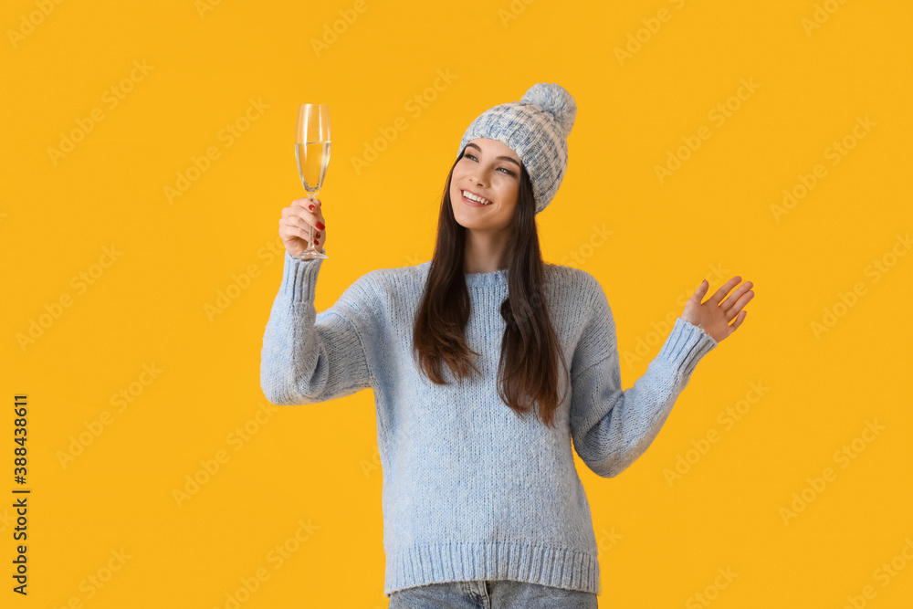 Beautiful young woman in winter clothes and with champagne on color background