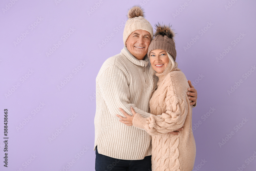 Mature couple in winter clothes on color background