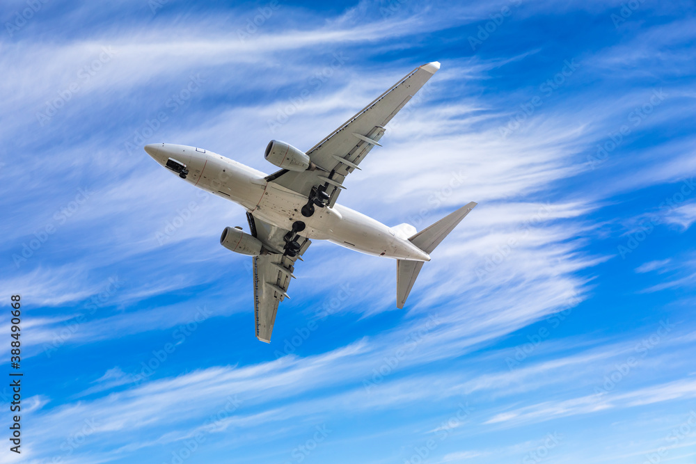 Commercial airplane flying above blue sky and white clouds.