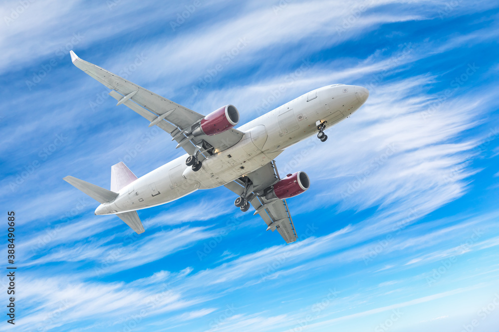 Commercial airplane flying above blue sky and white clouds.