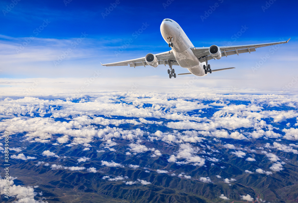 Commercial airplane flying above blue sky and white clouds.