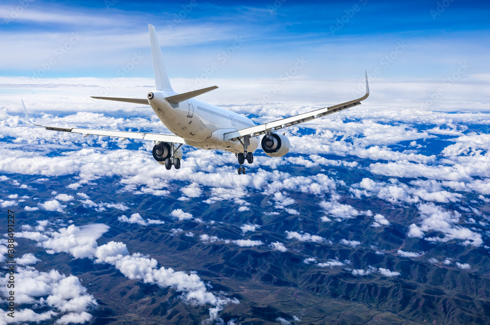 Commercial airplane flying above blue sky and white clouds.