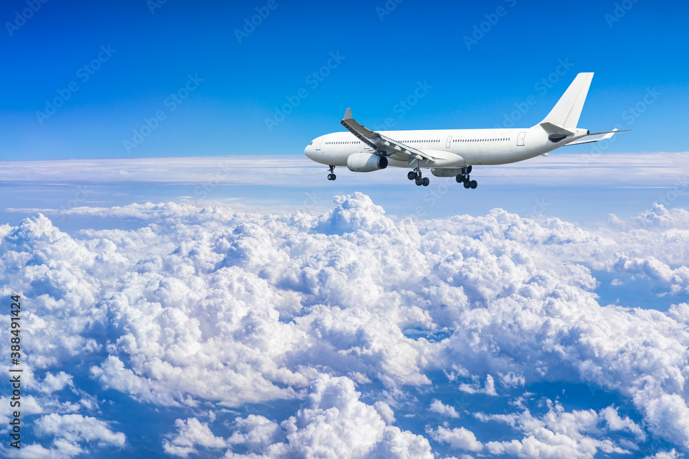 Commercial airplane flying above blue sky and white clouds.